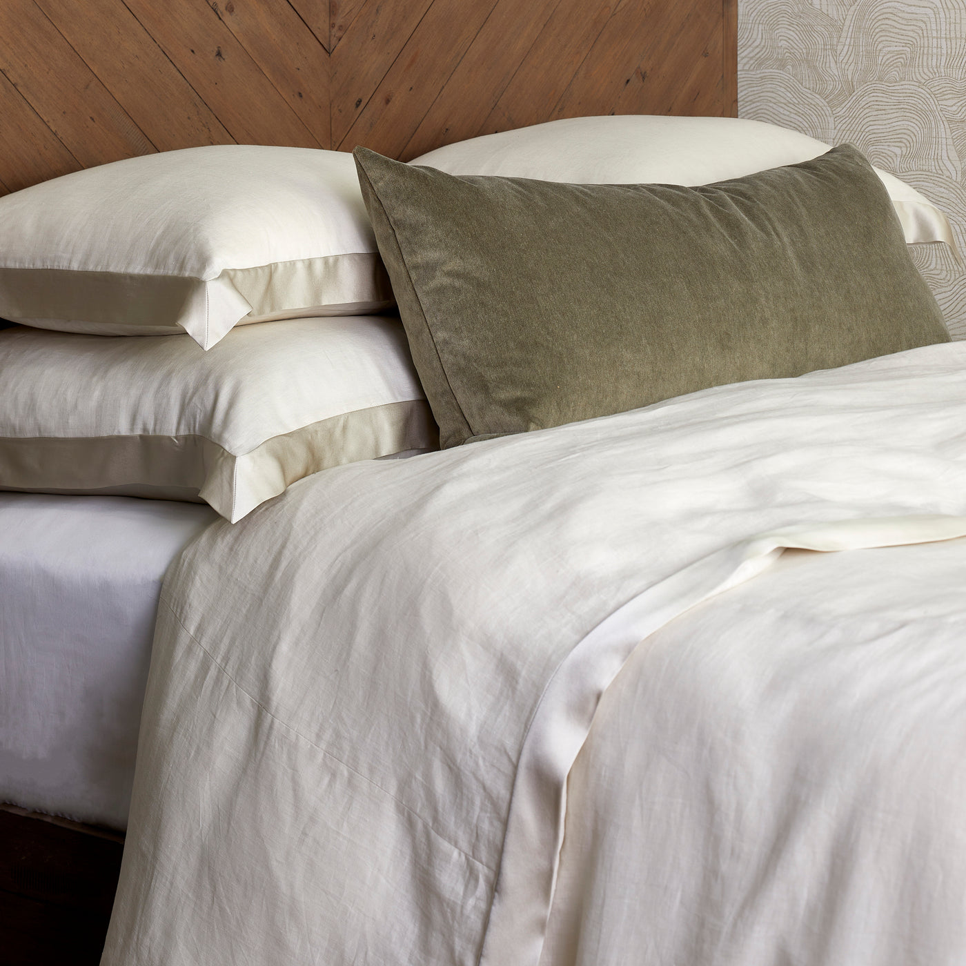 Ivory linen duvet with satin trim on a styled bed with olive velvet bolster pillow.
