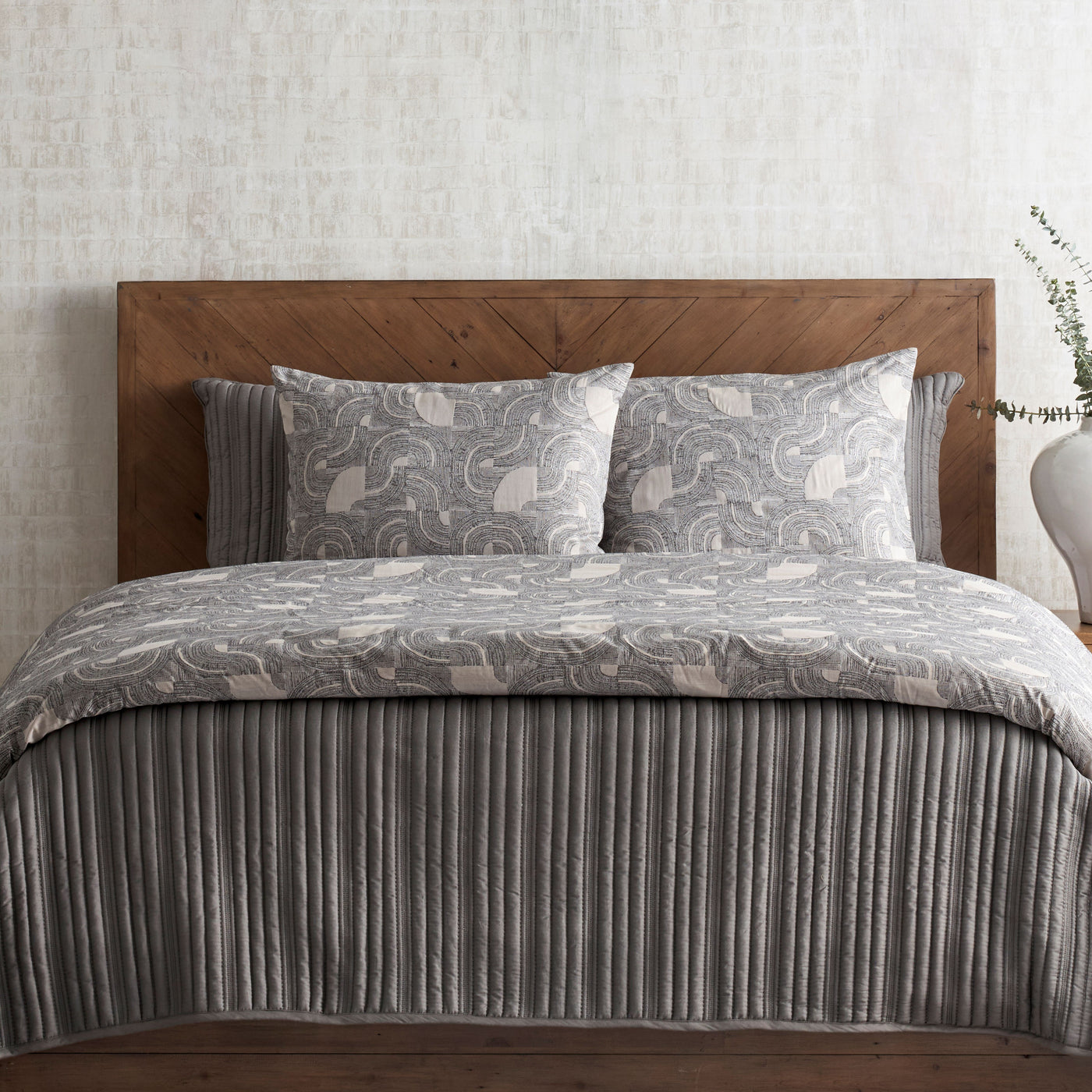 Lugano comforter set styled on bed, grey floral duvet with ribbed skirt, rustic wood headboard.