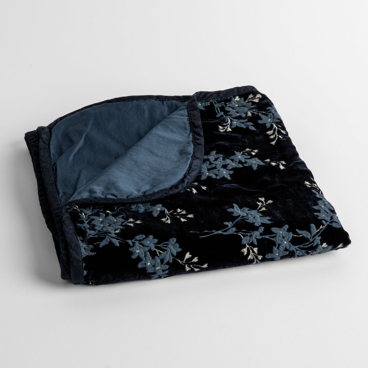 Folded Midnight velvet baby blanket showing floral pattern exterior and solid blue-grey lining.