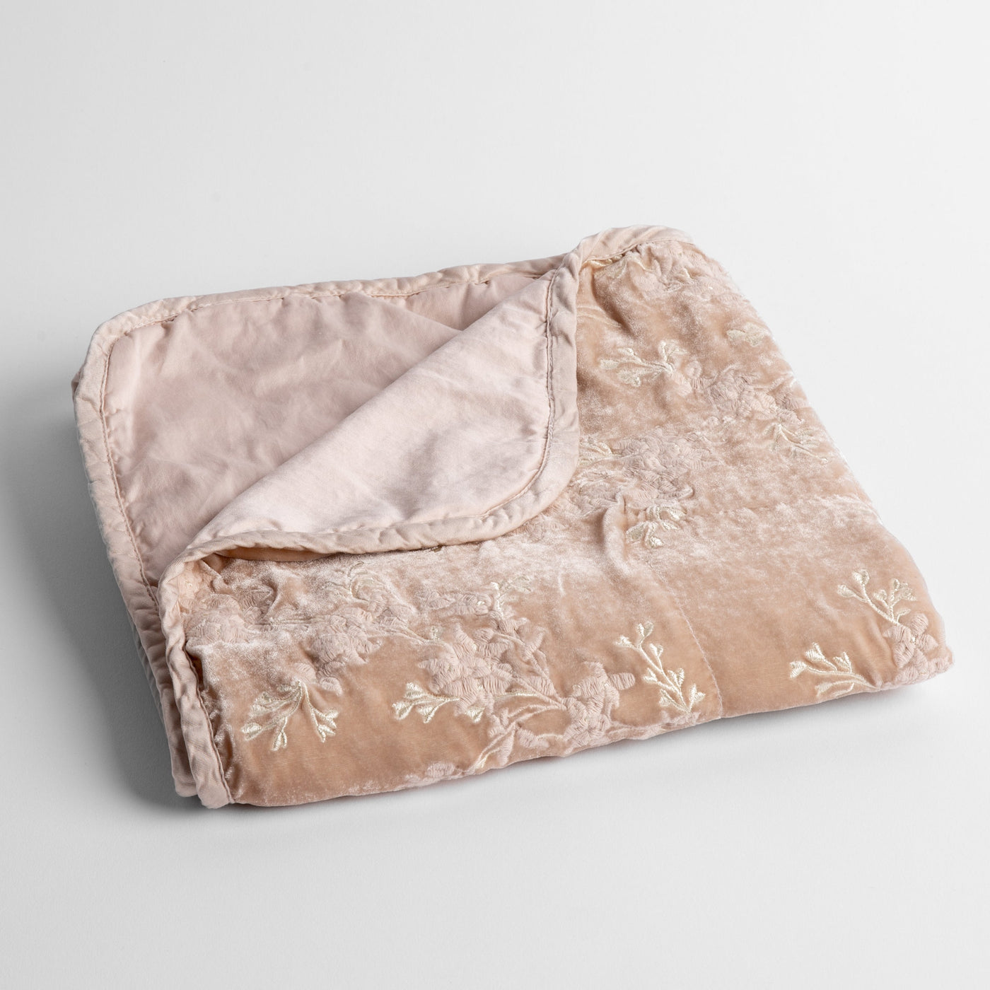Folded Pearl velvet baby blanket with white floral embroidery and contrast reverse.