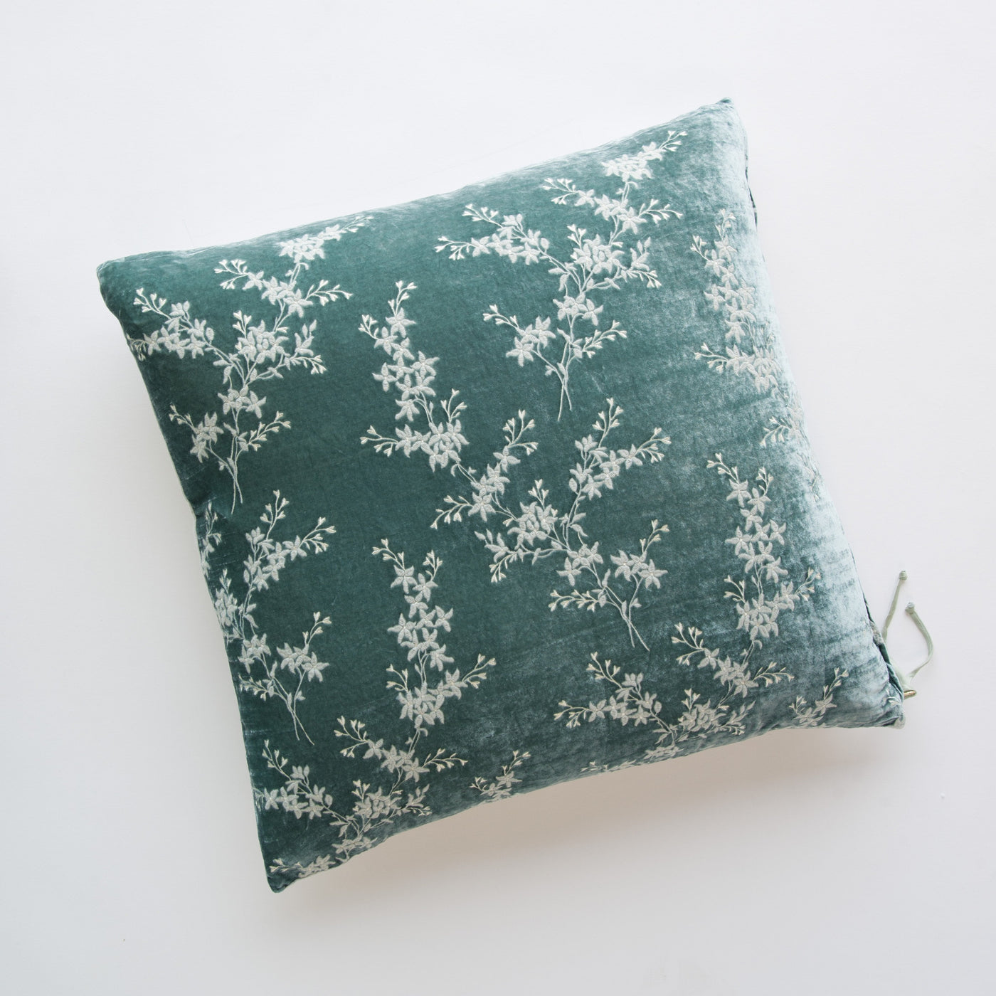 Eucalyptus velvet throw pillow with white floral branch embroidery, flat lay view.
