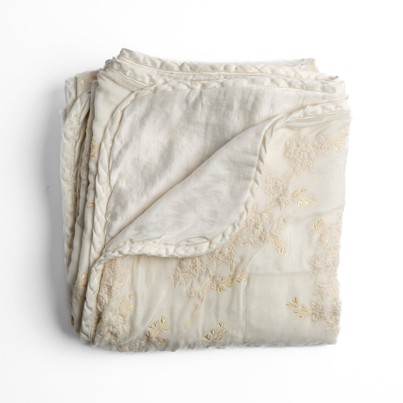 Bella Notte Lynette blanket in Winter White, folded to show floral embroidery and braided trim detail.