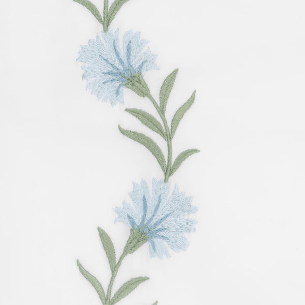 Close-up of powder blue cornflower embroidery with sage green stems on white linen.