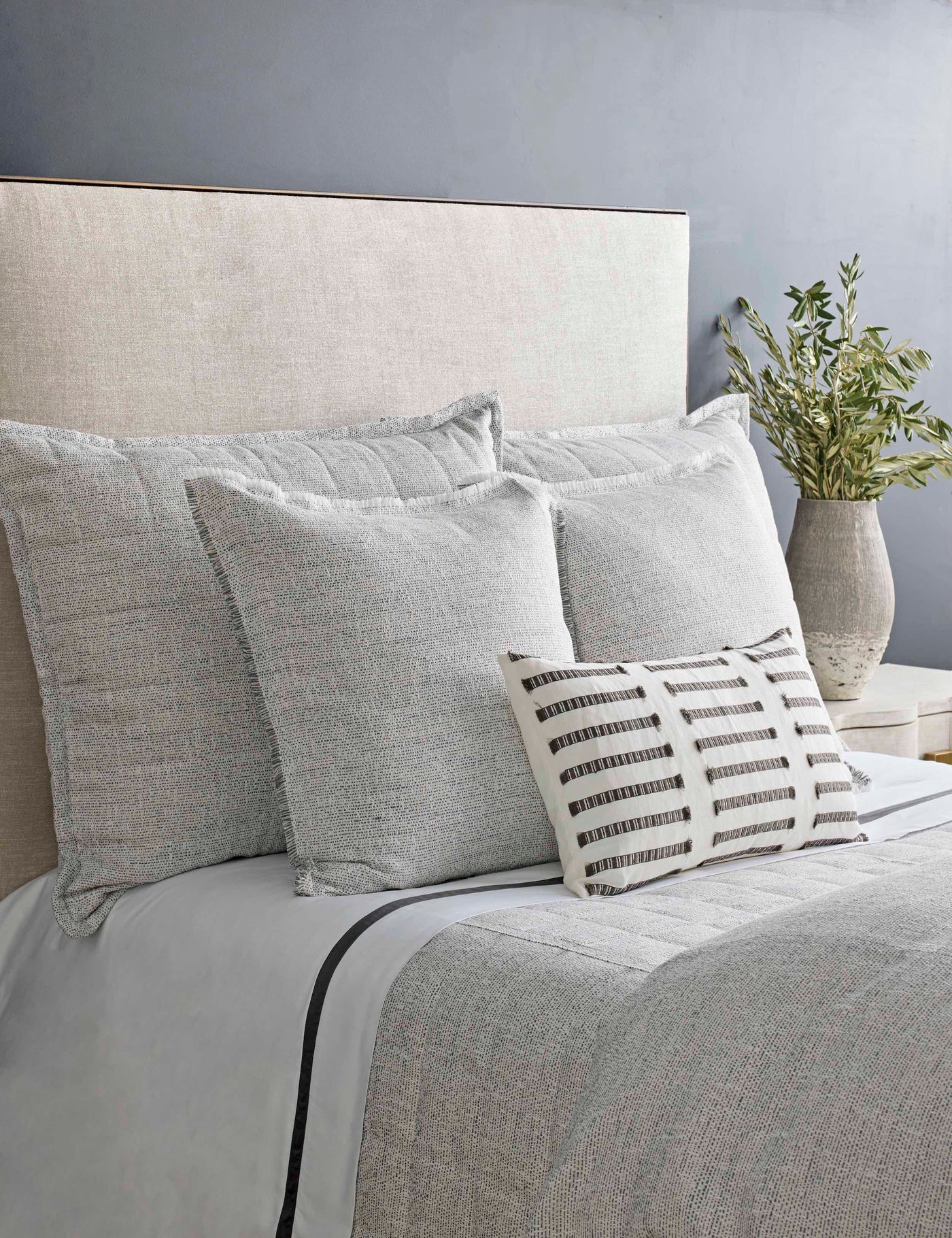Styled bed with grey textured duvet and euro shams, small striped lumbar pillow accent.