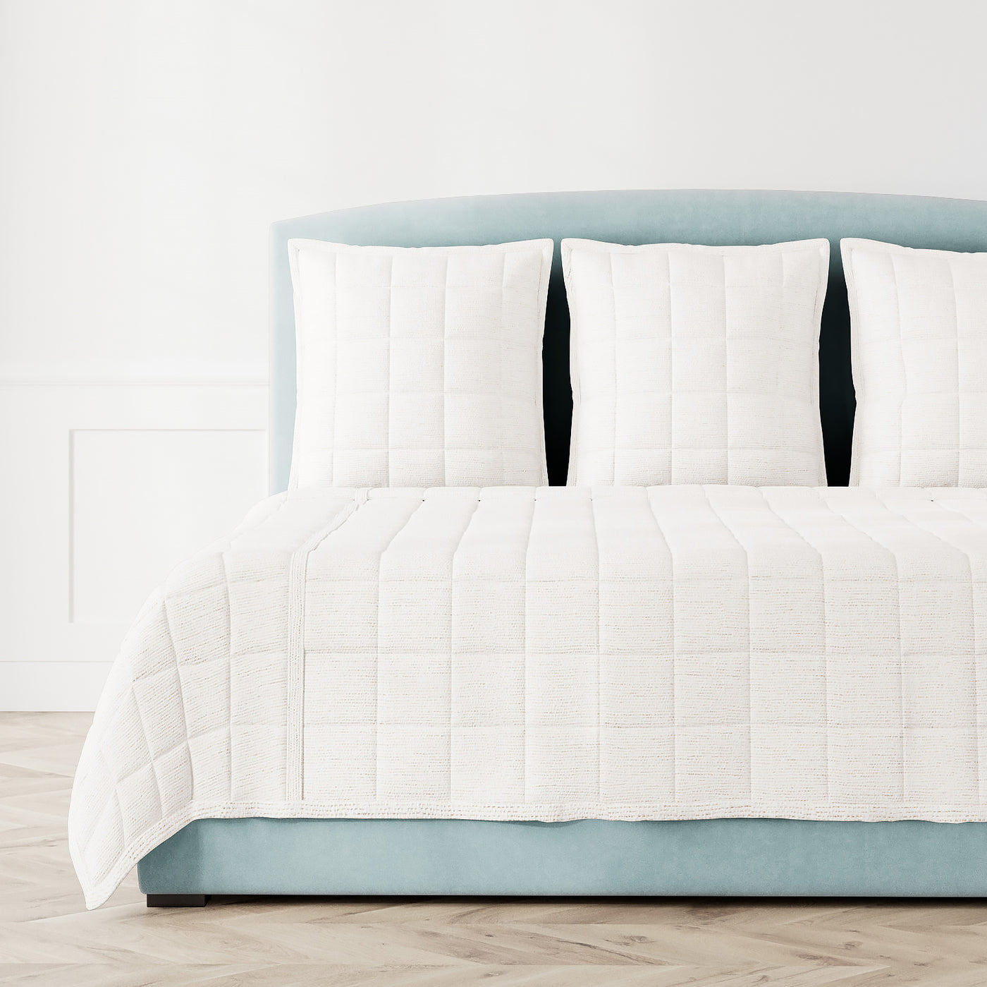 Ann Gish Macau coverlet and shams in ivory, styled on a blue upholstered bed.