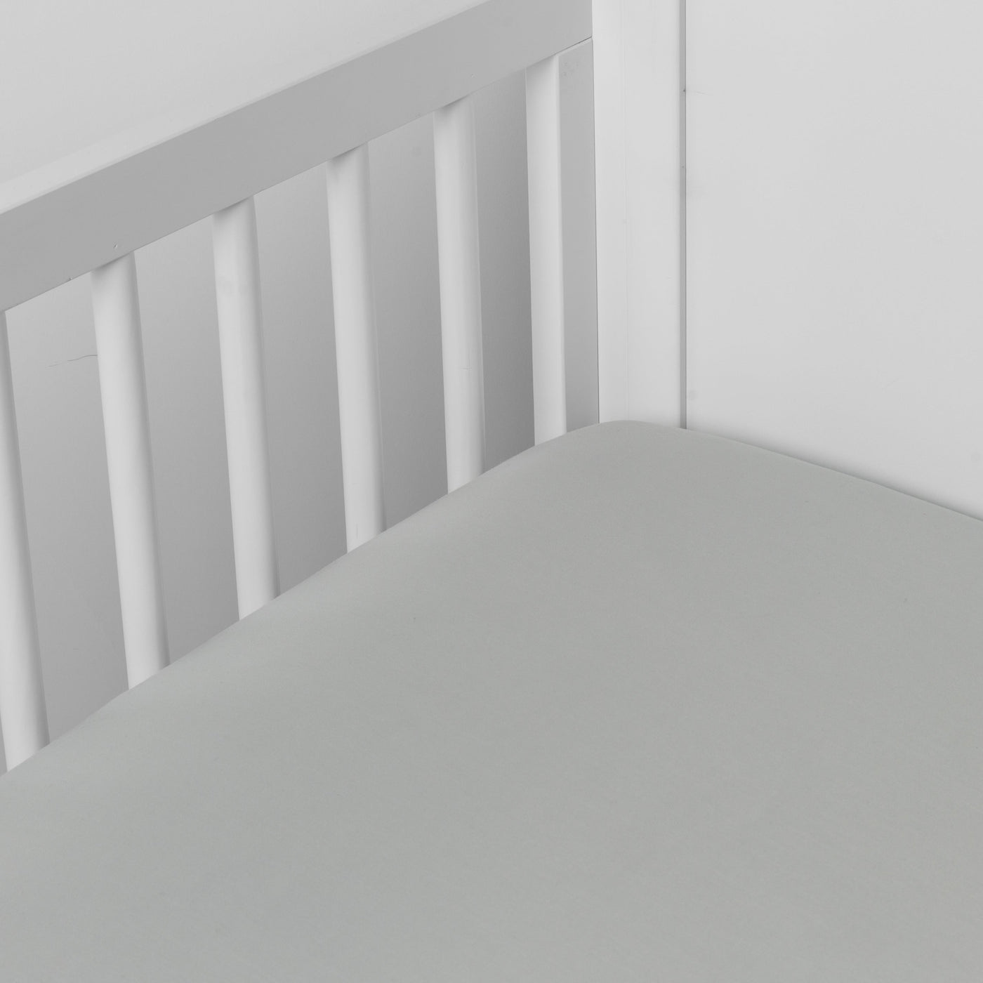 Madera Luxe crib sheet in soft grey, fitted smoothly in a white slatted crib.