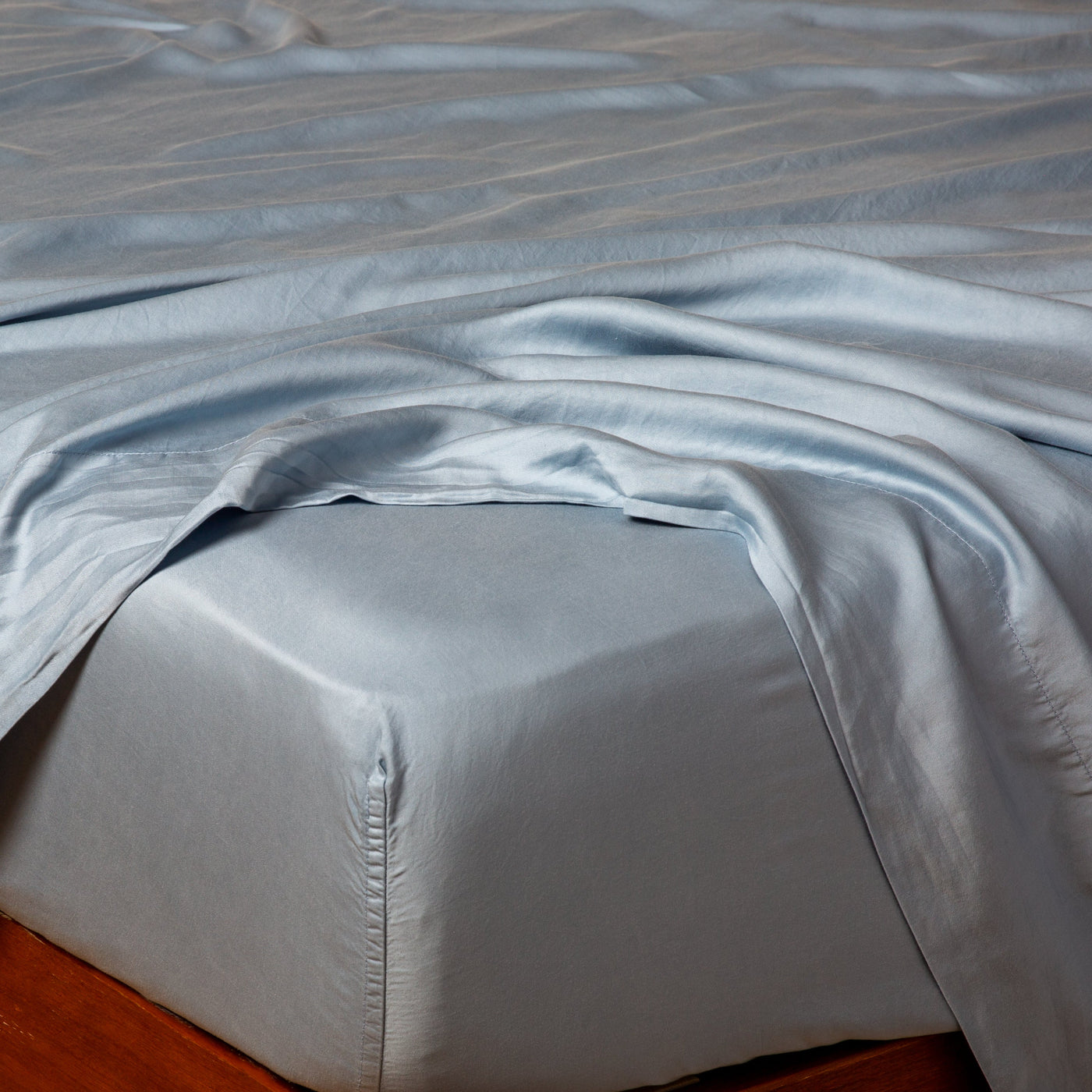 Fitted sheet corner on wood bed frame, Tahoe Blue silky fabric draped loosely across mattress.