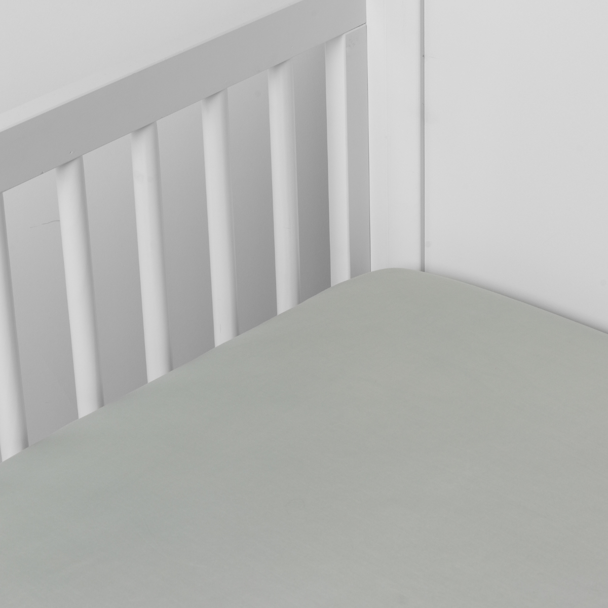 Eucalyptus fitted crib sheet shown smooth on a grey slatted crib mattress.