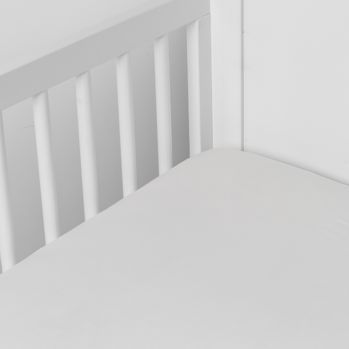 Winter White crib sheet fitted snugly on a white slatted crib, corner detail visible.