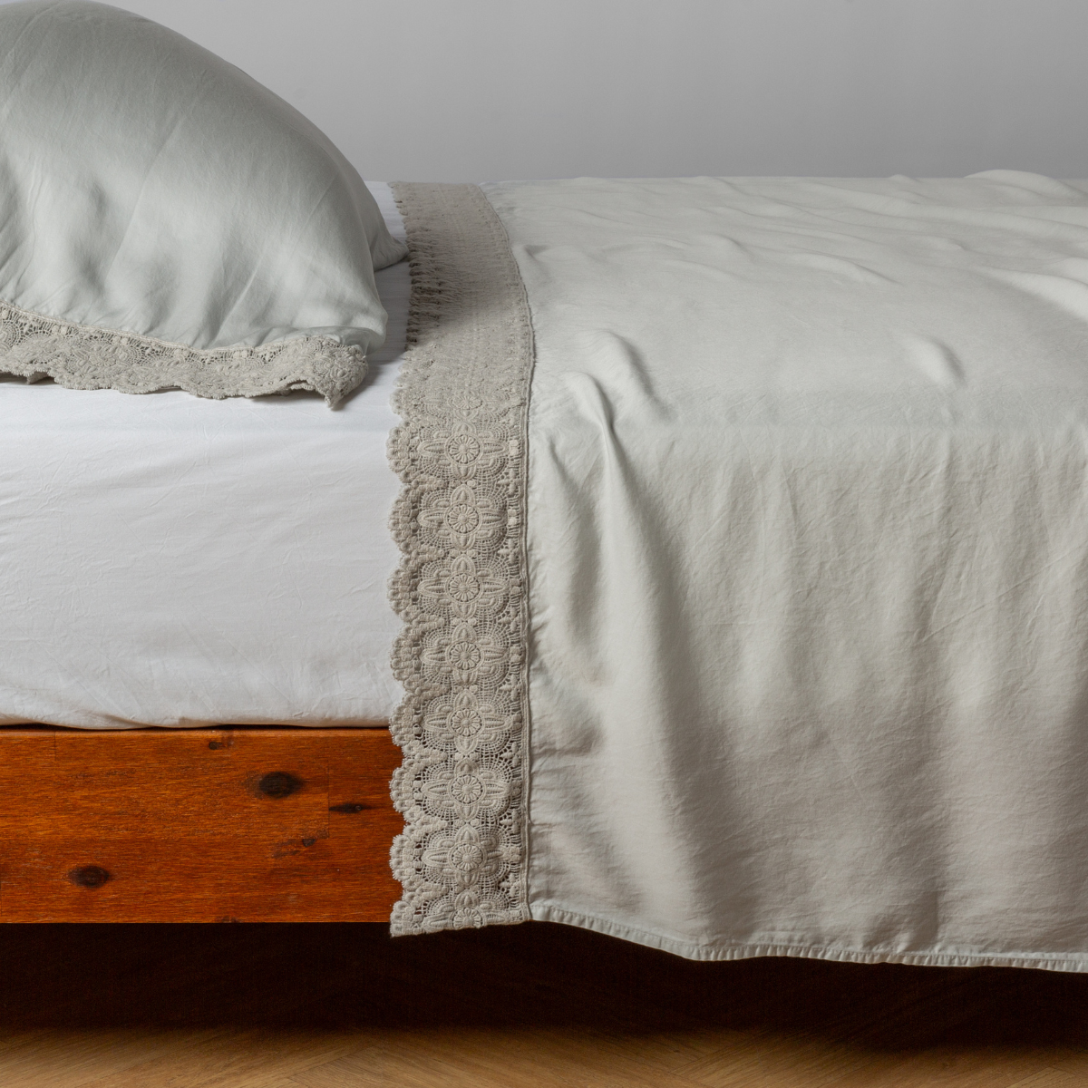 Flat sheet in Cloud draped over bed, showing crochet lace trim detail along the top edge.