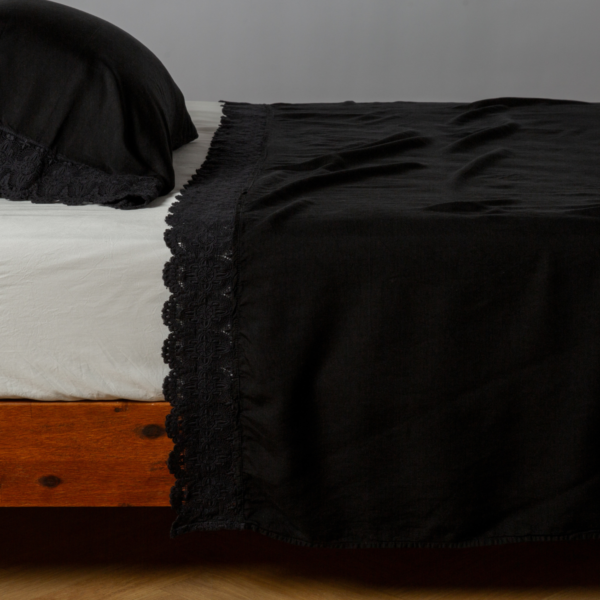 Corvino flat sheet draped over bed, black lace trim detail visible along edge.