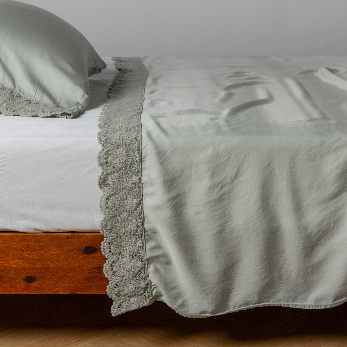 Eucalyptus flat sheet draped over bed, showing delicate lace trim detail along the folded edge.