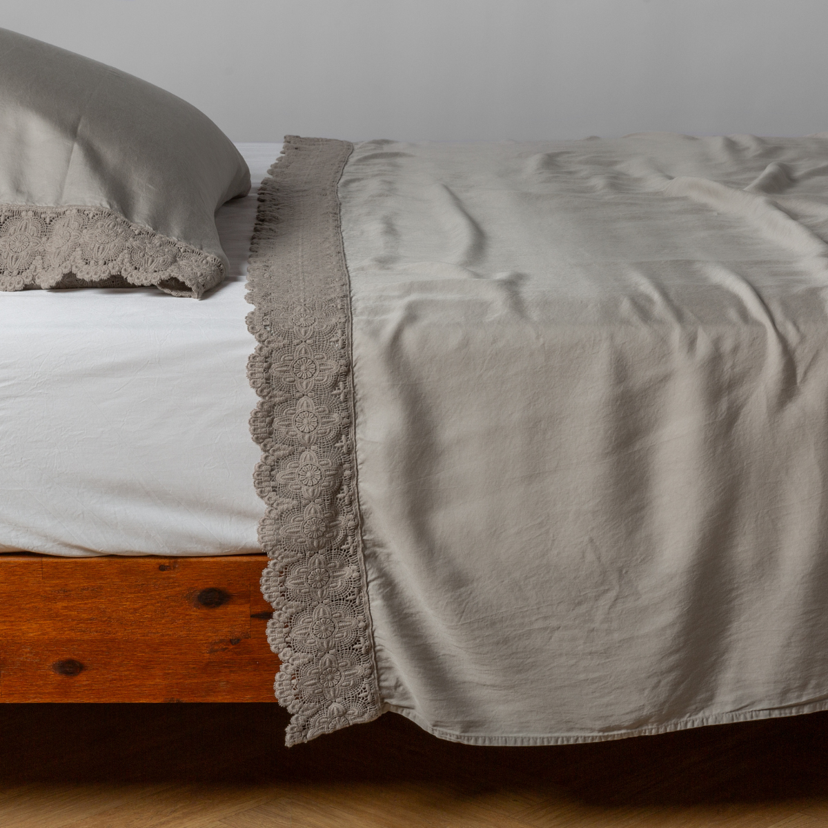 Flat sheet and pillowcase in Fog draped over bed, showing scalloped lace trim detail.