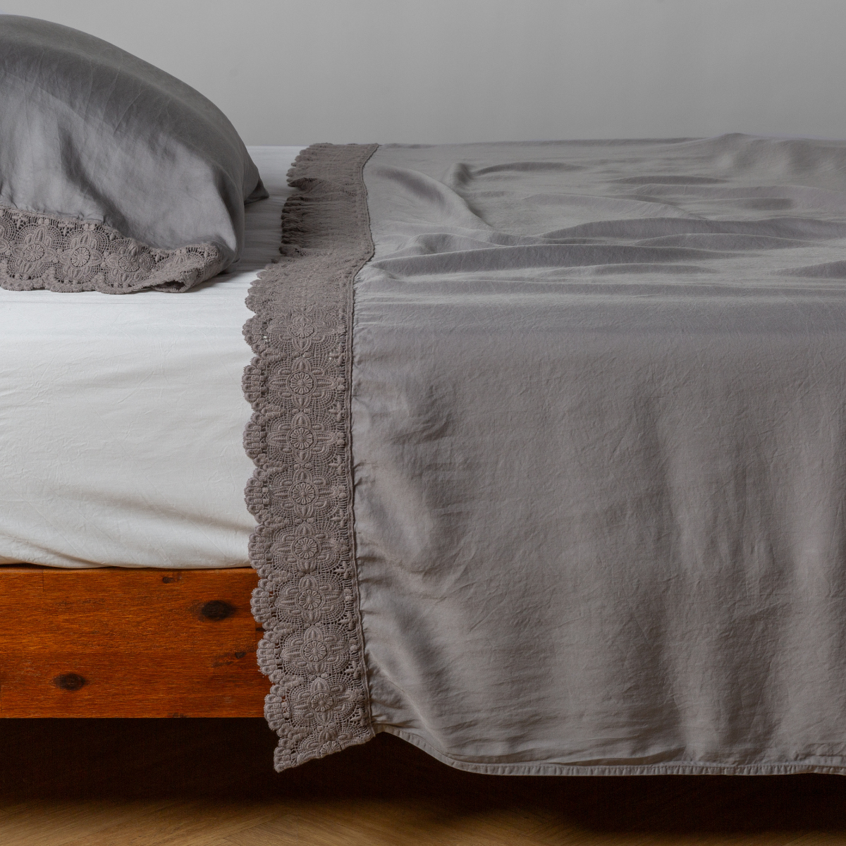 Madera Luxe flat sheet in French Lavender with floral lace trim, draped over a wood-frame bed.