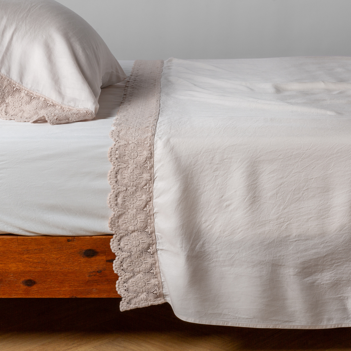 Pearl Madera Luxe flat sheet with delicate lace trim, draped over a wooden bed frame.