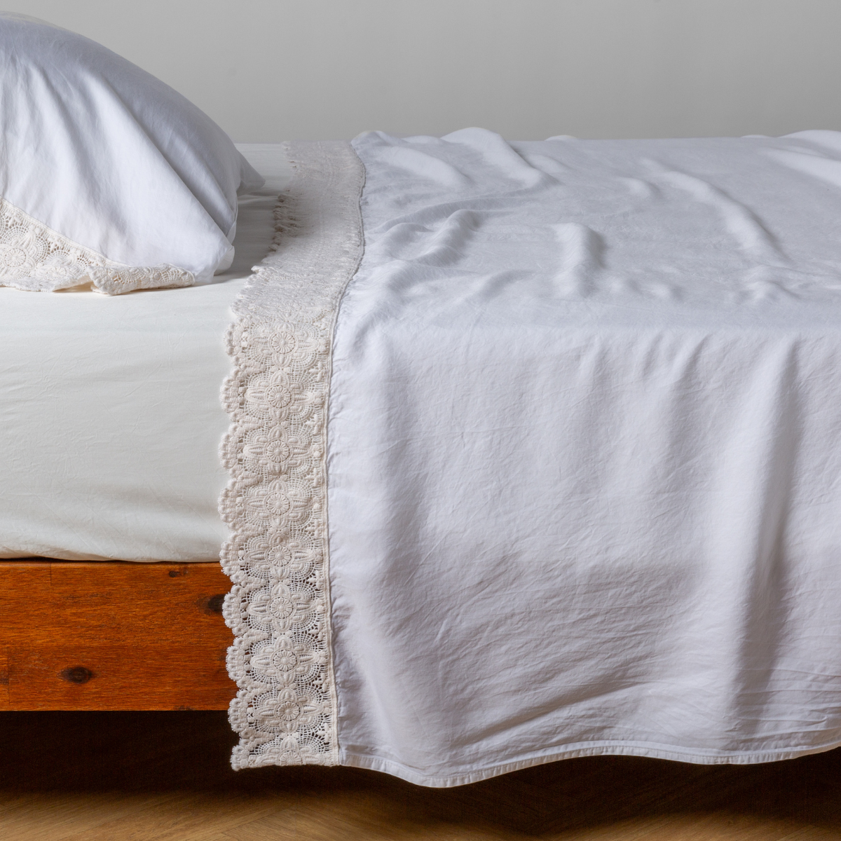 White Madera Luxe flat sheet folded back, showing delicate lace trim detail on wooden bed frame.