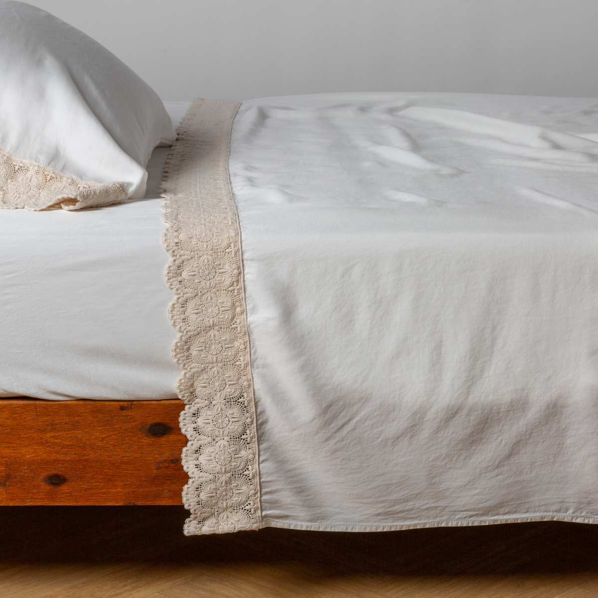 Flat sheet draped over bed, Winter White linen border with scalloped lace trim detail visible.