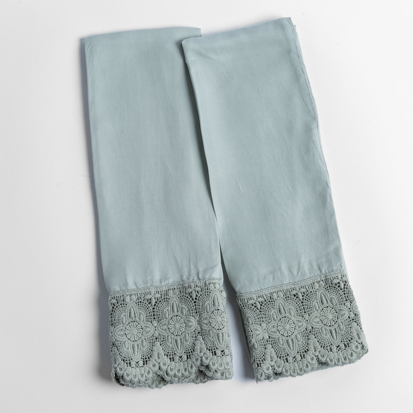 Eucalyptus lace-trimmed pillowcase pair laid flat, showing ornate floral crochet hem detail.