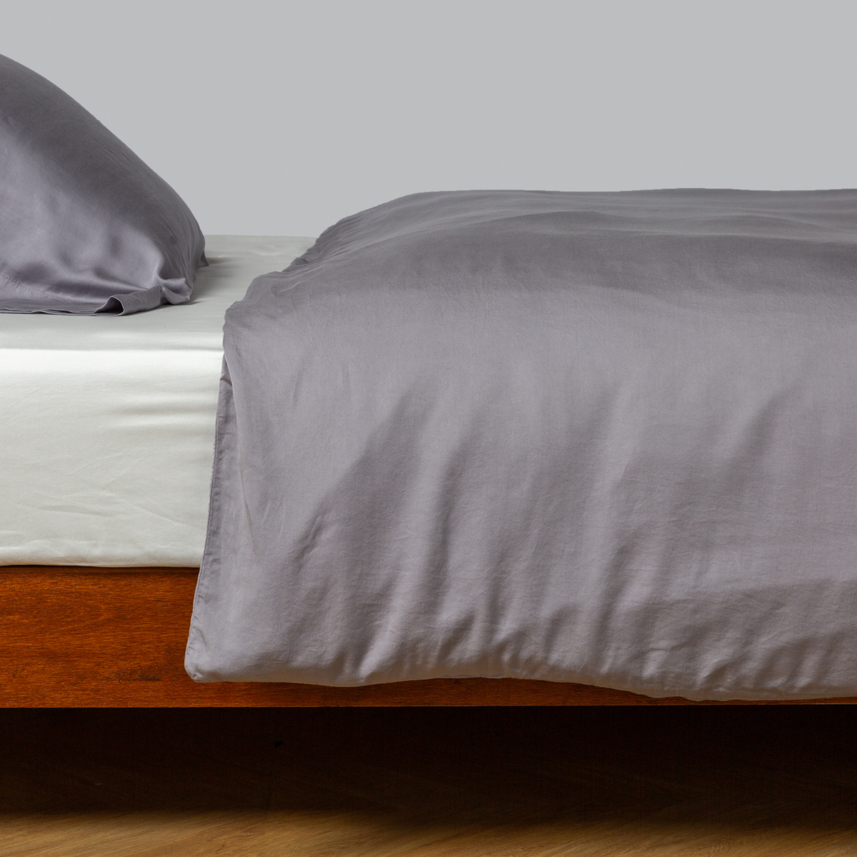 Slate-toned French Lavender duvet cover draped over bed with matching pillowcase, warm wood frame.