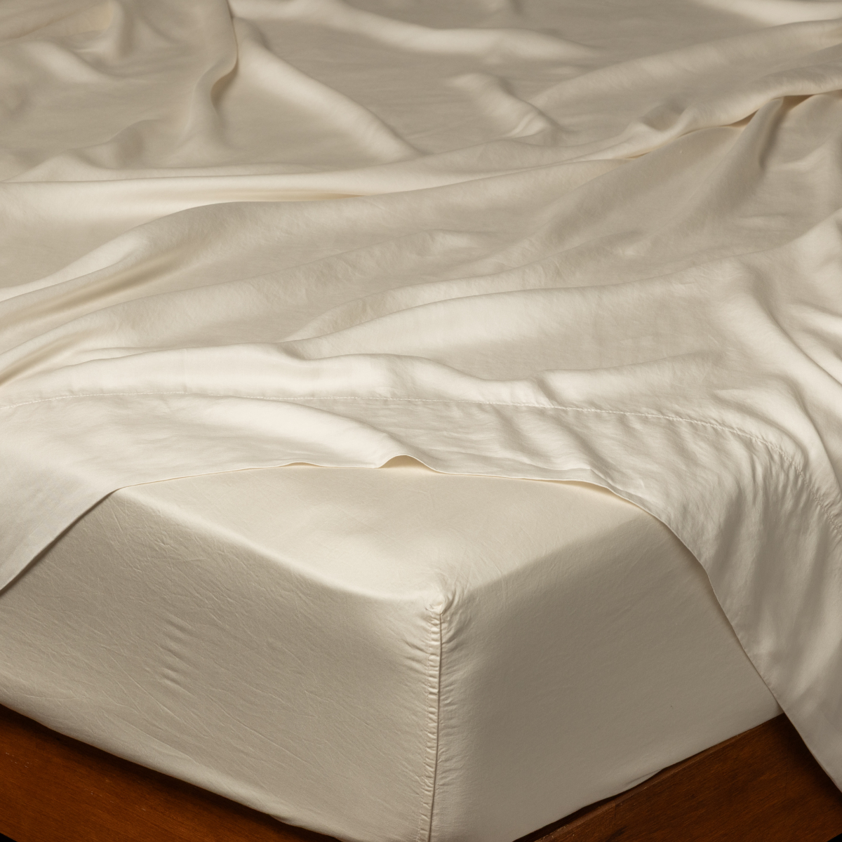 Bella Notte Madera Luxe fitted sheet in Natural, draped loosely over a wood-framed bed.