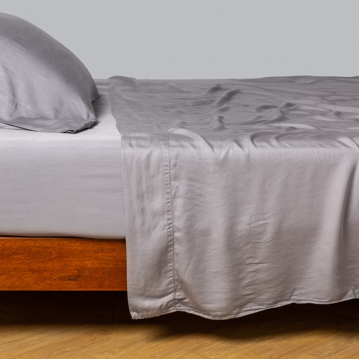 Madera Luxe flat sheet in French Lavender draped loosely over a wood-frame bed, full side view.