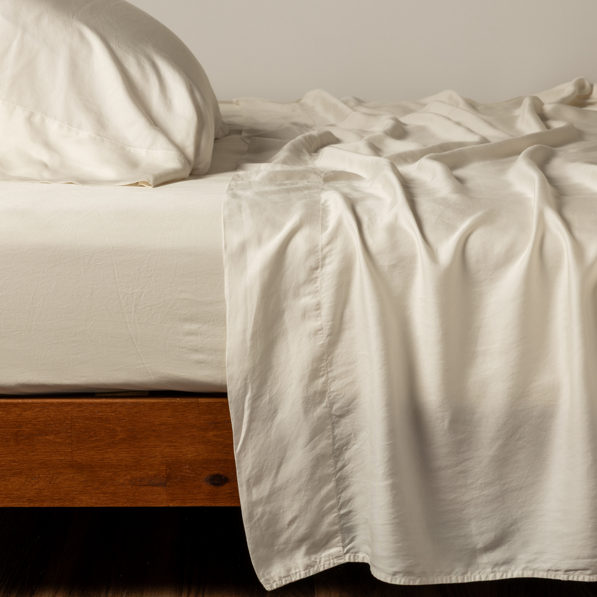 Bella Notte Madera Luxe flat sheet in Natural draped over wood bed frame, ivory satin sheen.