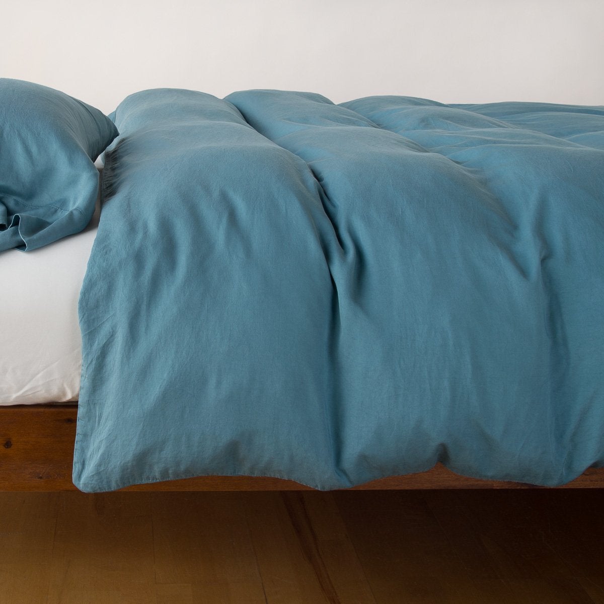 Angled view of Bella Notte Madera Luxe duvet cover draped over a bed, showing soft fabric drape.