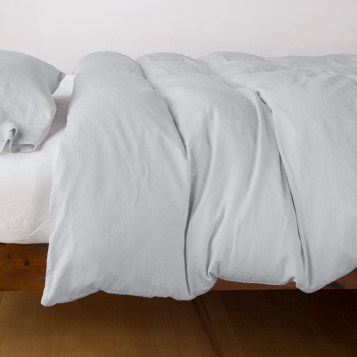 Bella Notte Madera Luxe duvet cover in Cloud, draped loosely over a wood-frame bed.