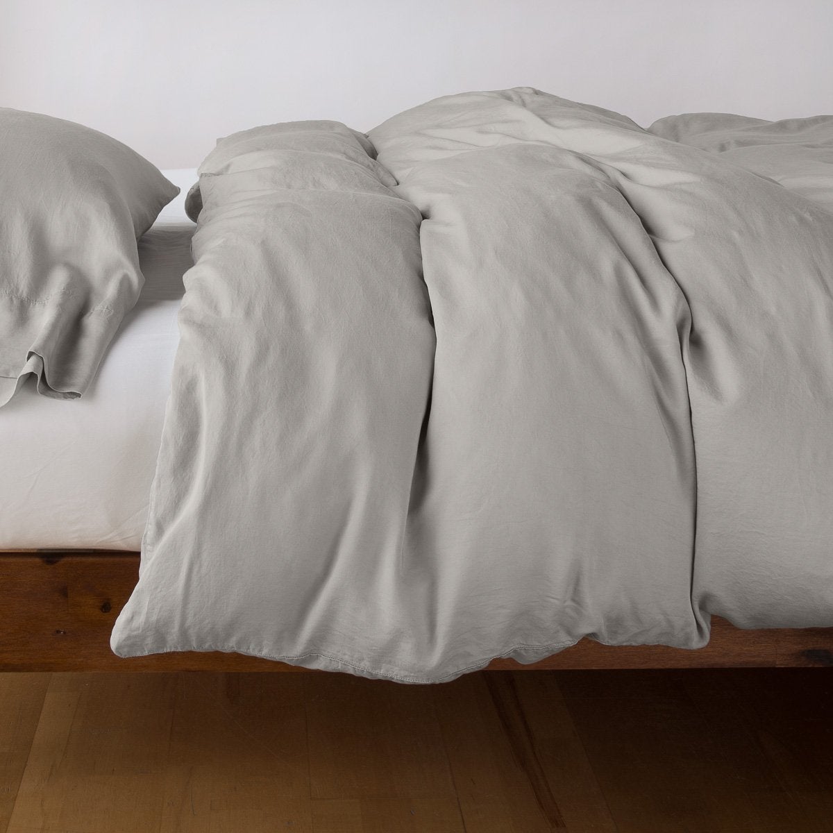 Fog duvet cover and pillowcases draped on a wood-frame bed, soft relaxed fabric with natural folds.