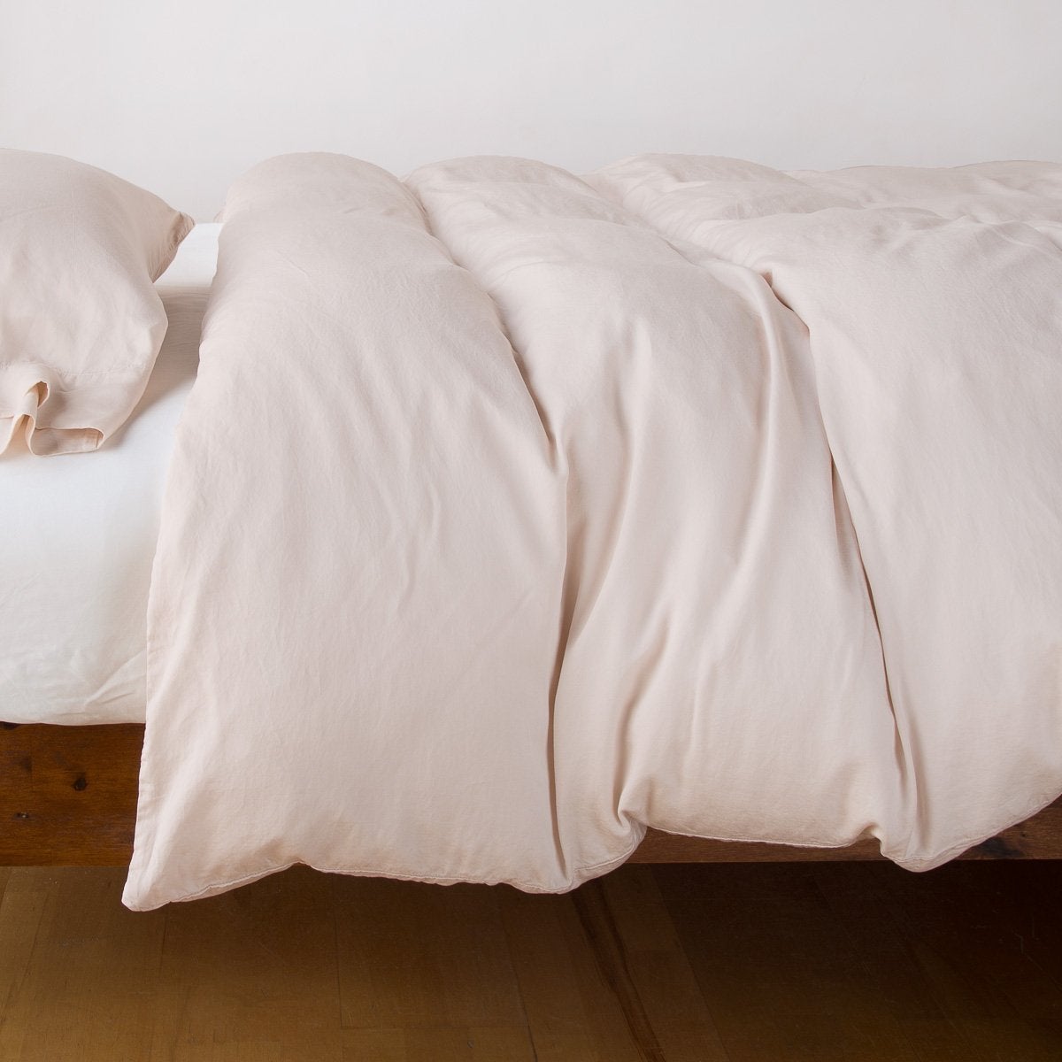 Bella Notte Madera Luxe duvet cover in Pearl, draped softly over a wooden bed frame.