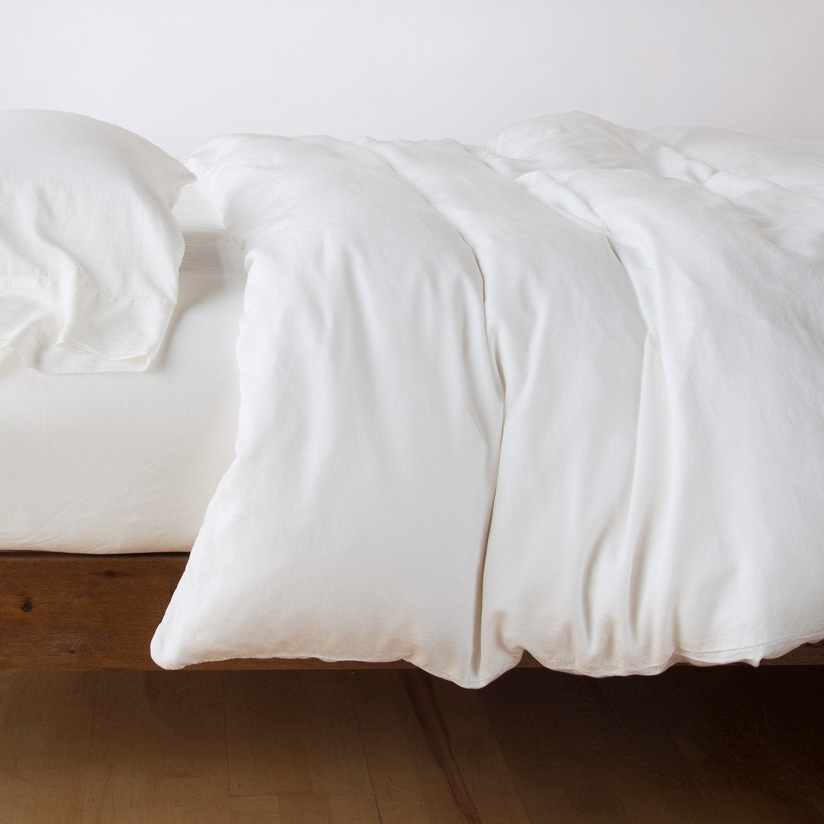 Bella Notte Madera Luxe duvet cover in Winter White, softly rumpled on a low wood-frame bed.