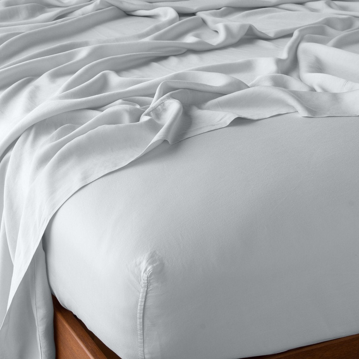 Draped Cloud fitted sheet on wood bed frame, showing silky smooth Madera Luxe fabric texture.