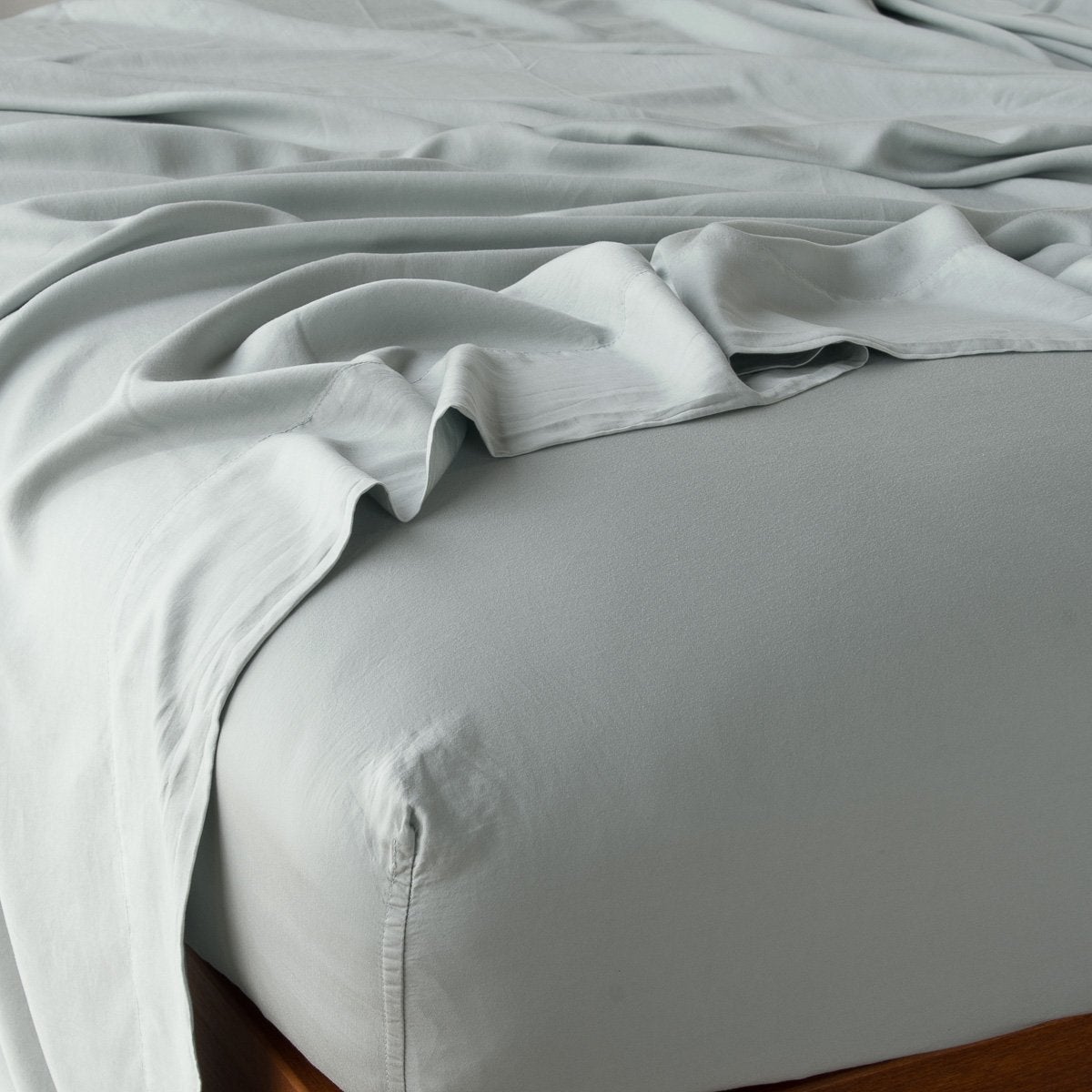 Eucalyptus fitted sheet draped loosely over a wood-frame bed, soft sheen visible on fabric.