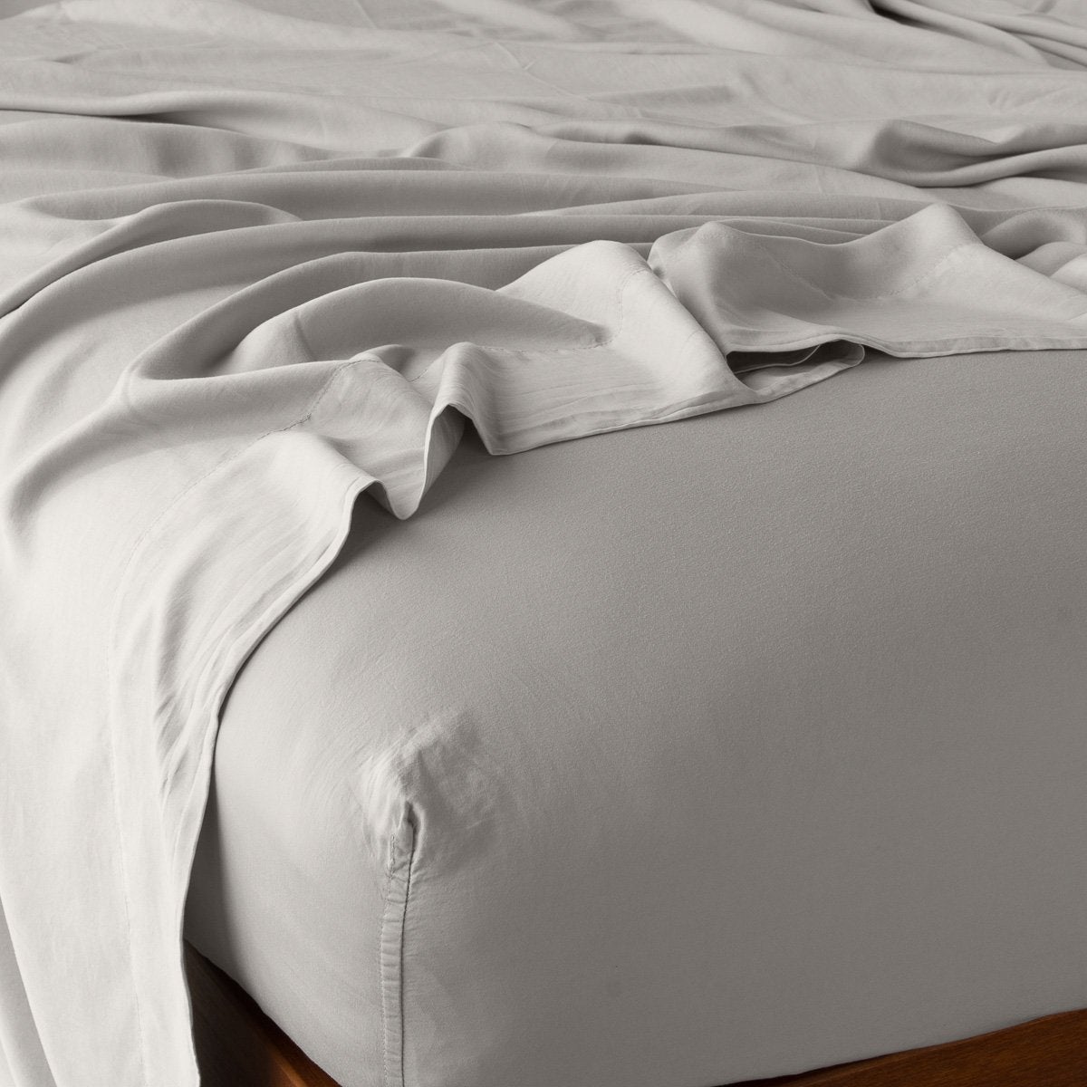 Fog fitted sheet with loosely draped flat sheet, showing soft drape on wood bed frame.