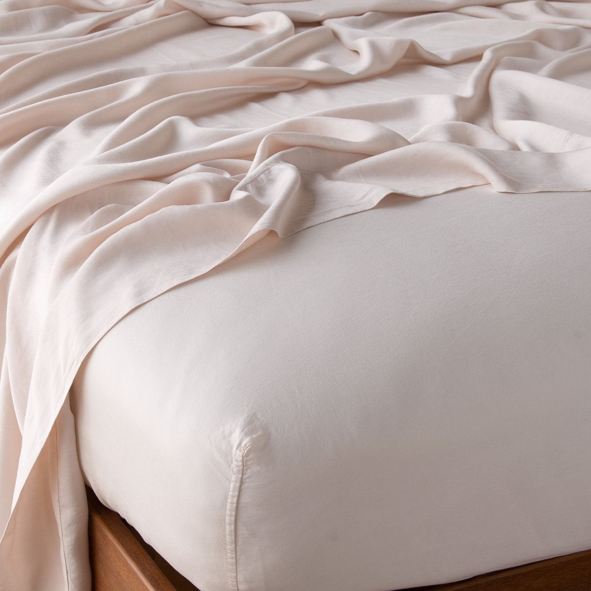 Close-up of Pearl fitted sheet corners on wood bed frame, with draped flat sheet above.