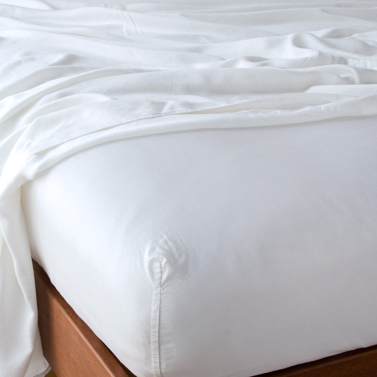 Bella Notte Madera Luxe fitted sheet in White, draped on a bed with a wood frame.