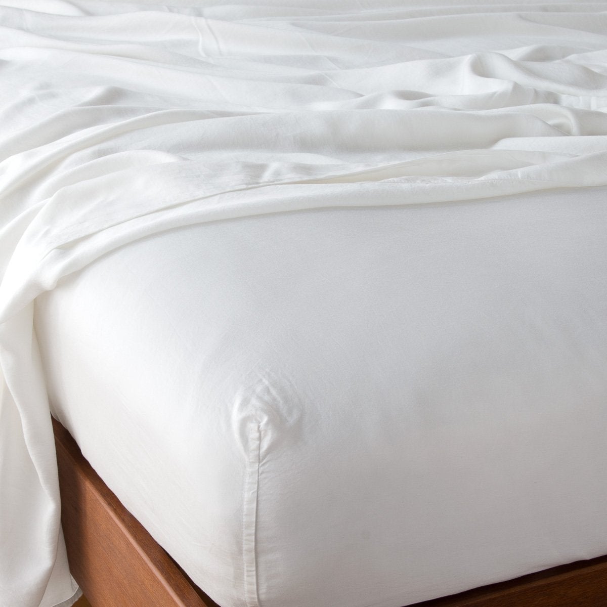 Winter White fitted sheet tucked smoothly over mattress on wood bed frame, soft draping flat sheet above.