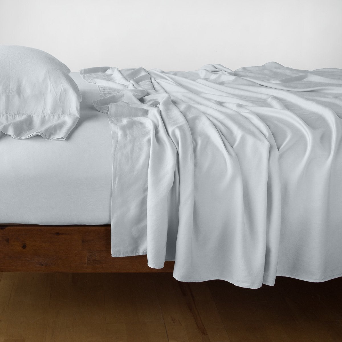 Madera Luxe flat sheet in Cloud draped over bed edge, showing lustrous fabric drape.