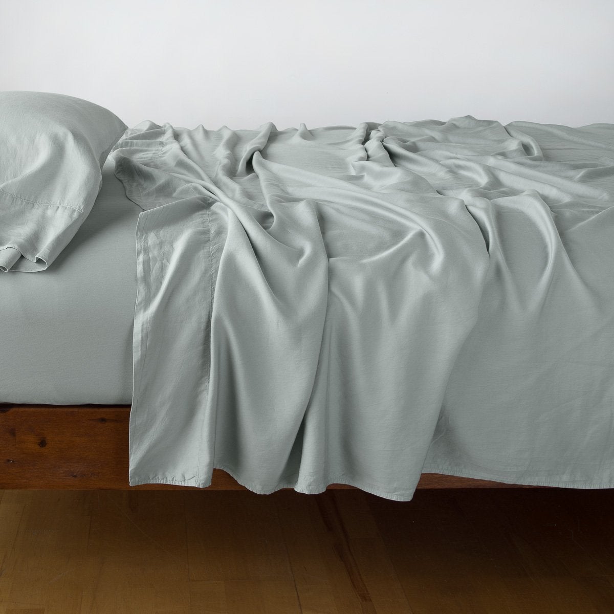 Eucalyptus flat sheet draped loosely over bed, showing fluid silky drape to the floor.