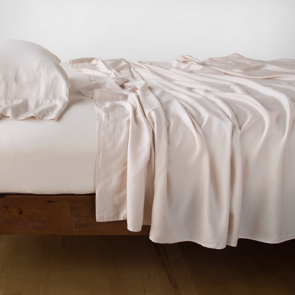 Bella Notte Madera Luxe flat sheet in Pearl draped loosely over a low wood bed frame.