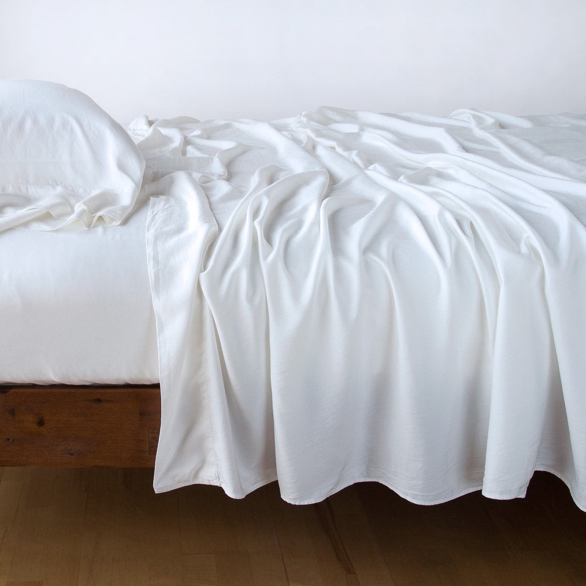 Bella Notte Madera Luxe flat sheet in White, draped loosely over a wood-frame bed.