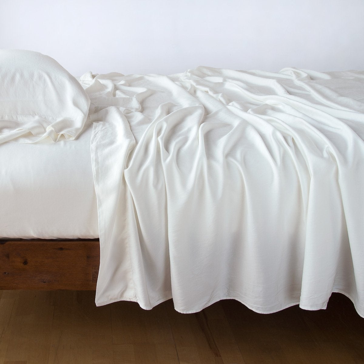 Bella Notte Madera Luxe flat sheet in Winter White draped loosely over a wood-framed bed.