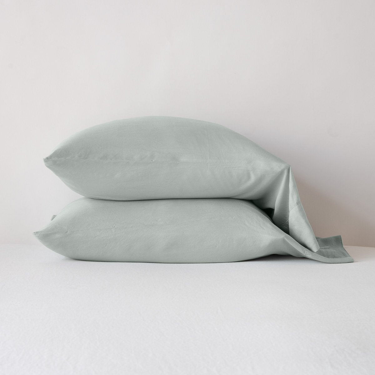 Two Bella Notte Madera Luxe pillowcases in Eucalyptus stacked on white bedding.