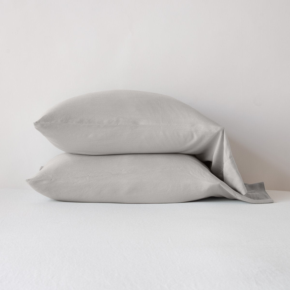 Two Bella Notte Madera Luxe pillowcases in Fog stacked against a white wall.