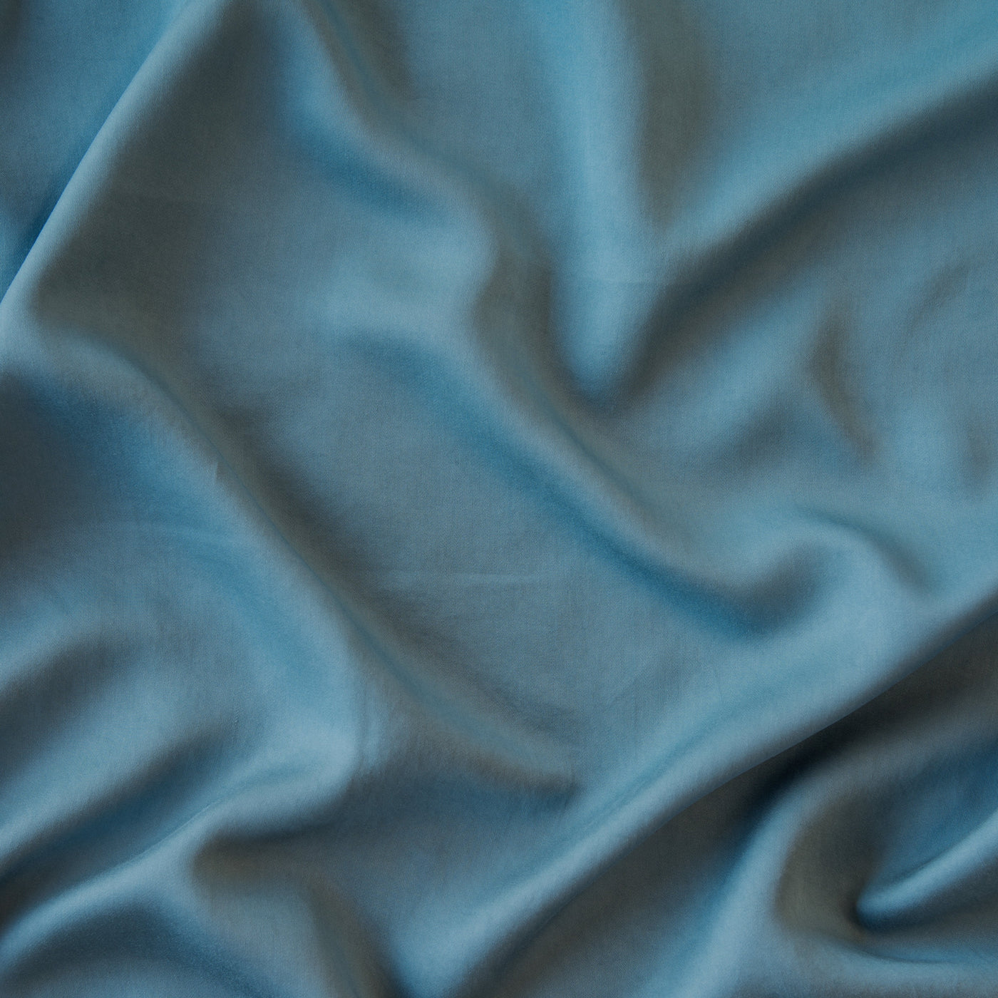 Close-up of draped steel blue Madera Luxe fabric showing smooth, lustrous texture.