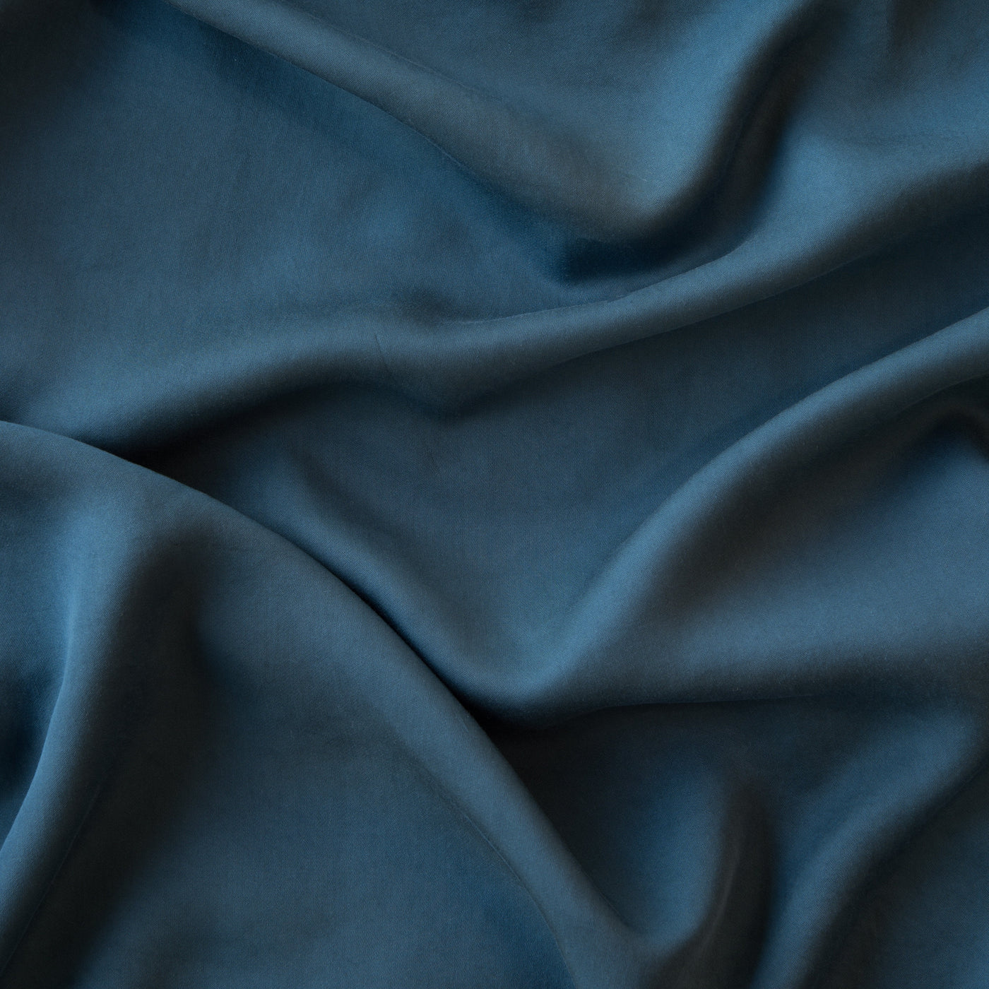Close-up of draped Madera Luxe fabric showing smooth, silky weave and deep teal tones.