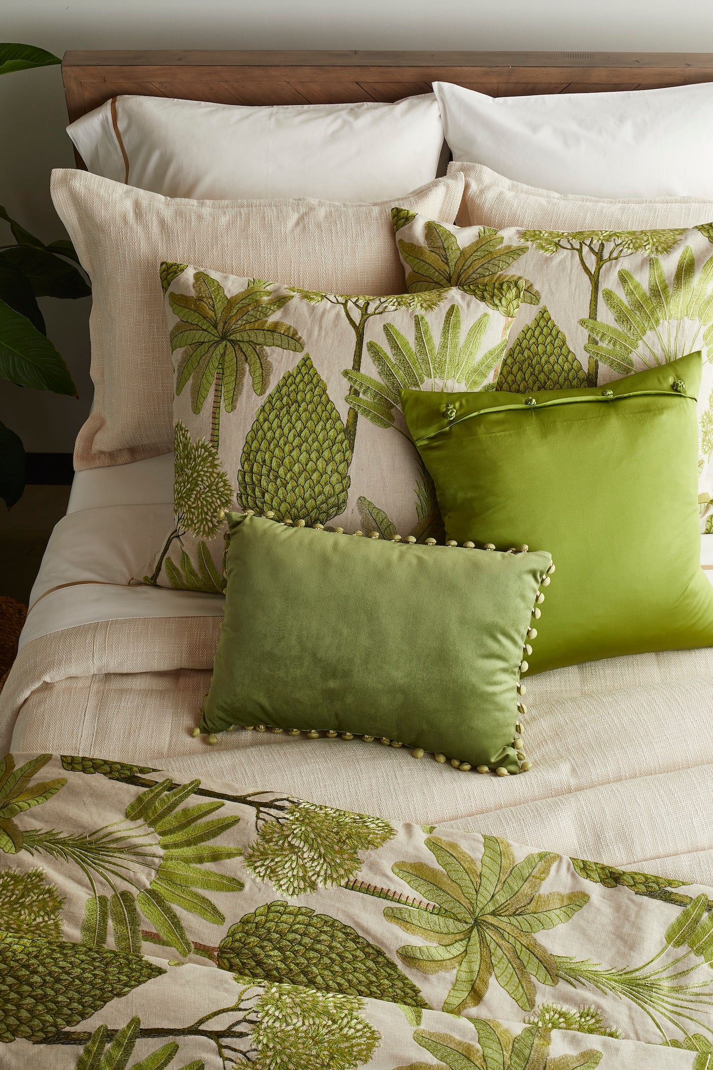 Green velvet lumbar pillow with pom-pom trim, styled on bed with tropical-print bedding.