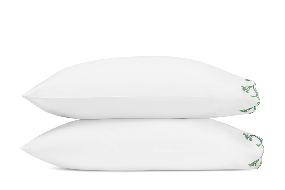 Two white Matouk Marcella pillowcases stacked, showing green embroidered vine detail at corner.