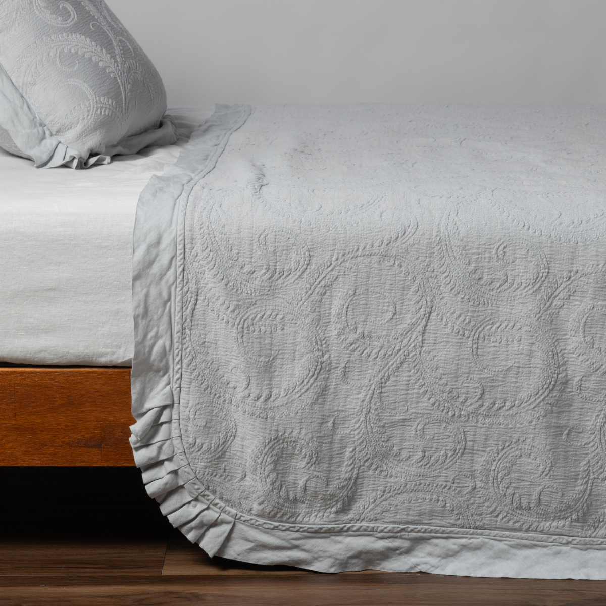 Cloud Marisette bedspread draped over bed corner, showing ruffled hem and paisley quilting detail.