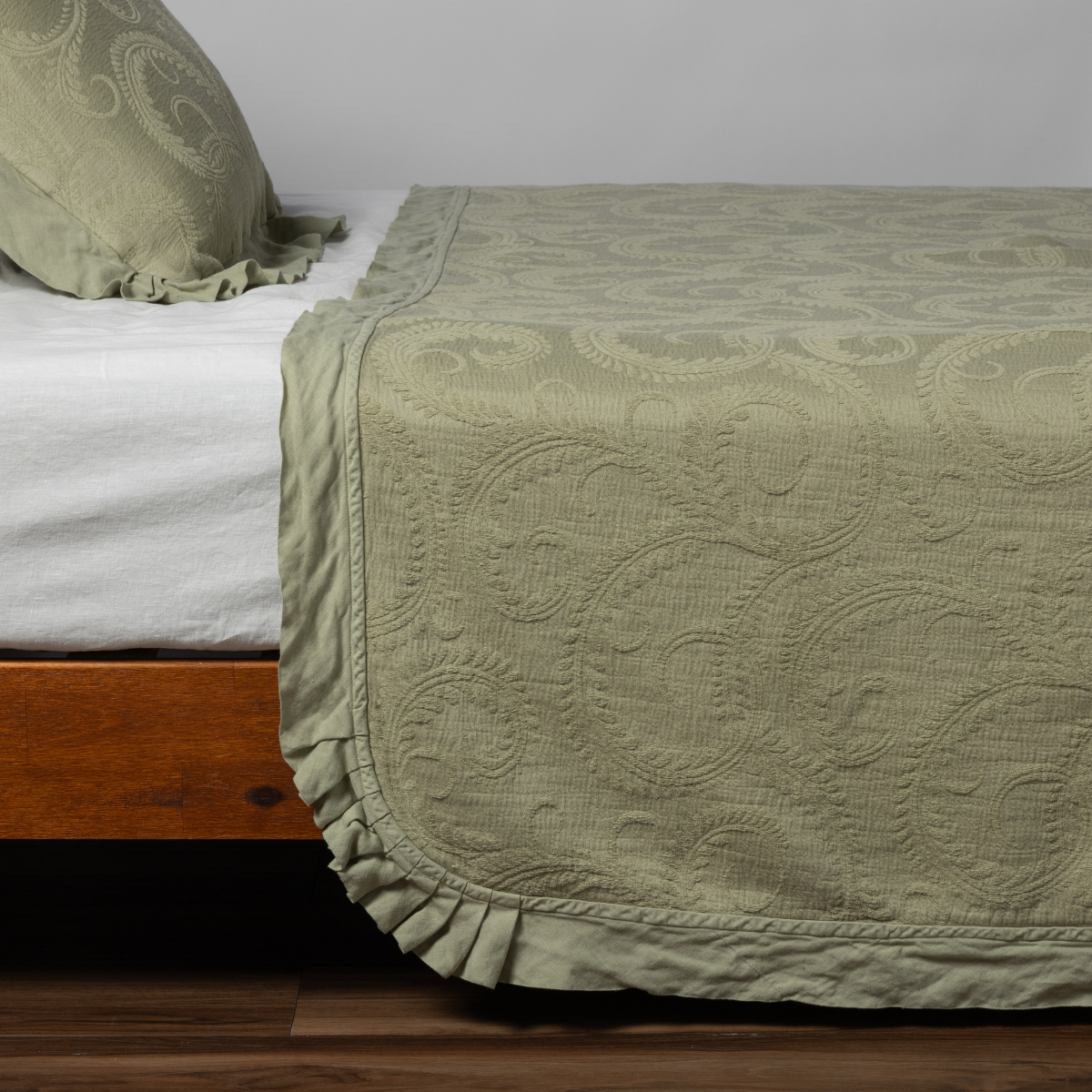 Desert Sage Marisette bedspread draped over bed foot, showing ruffled hem and paisley matelassé weave.